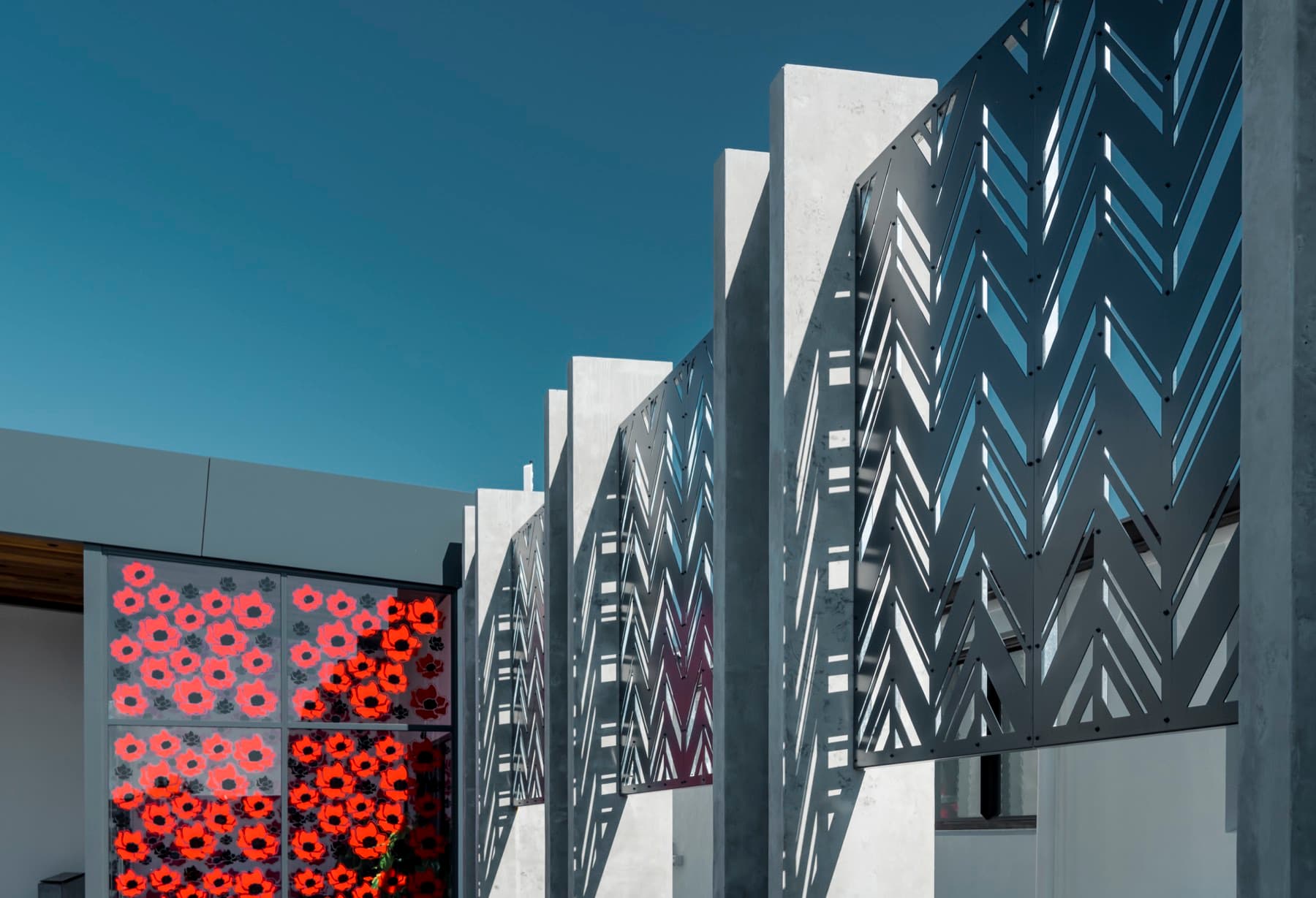 The exterior: laser-cut chevron screens fixed to precast concrete fins, with poppy-patterned glazing below.